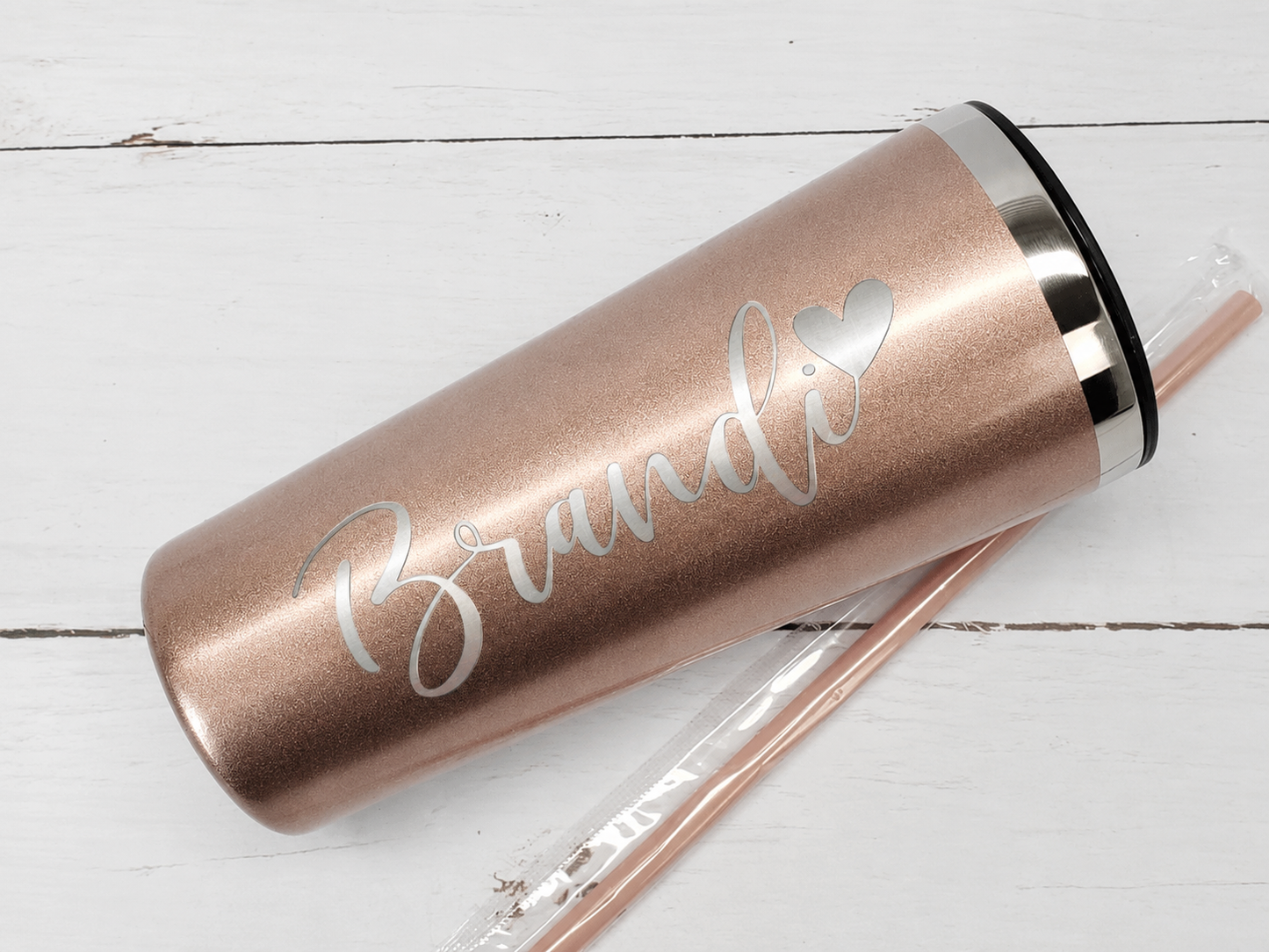 Rose gold tumbler with name and a heart on a white wooden surface